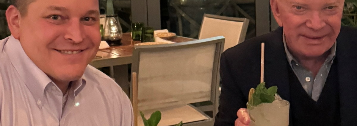 two men sitting at a table with food and drinks