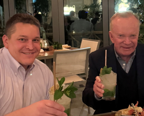 two men sitting at a table with food and drinks